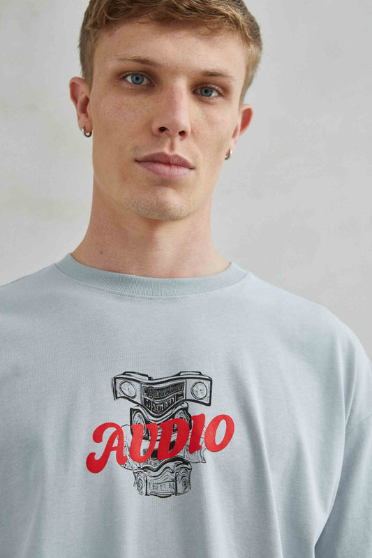 Camiseta oversize unisex gris con diseño gráfico "AUDIO" en el pecho.