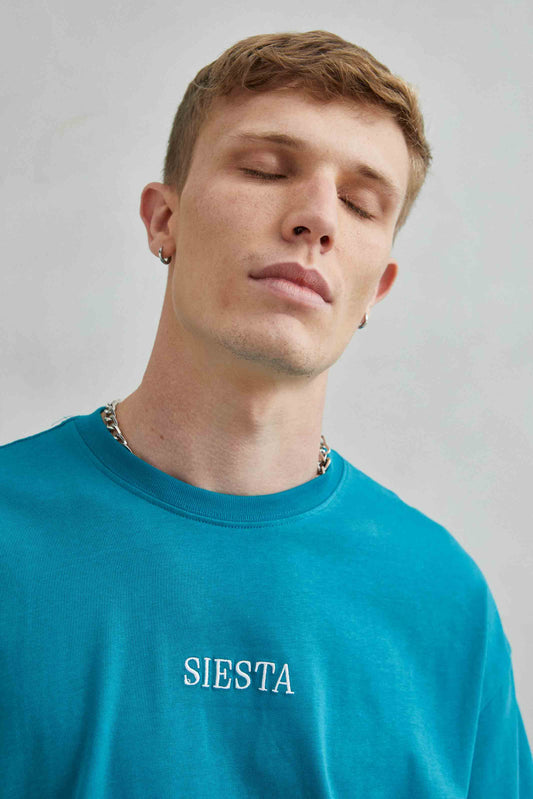 Detalle de camiseta verde oversize con texto bordado "Siesta" y diseño de koala durmiendo