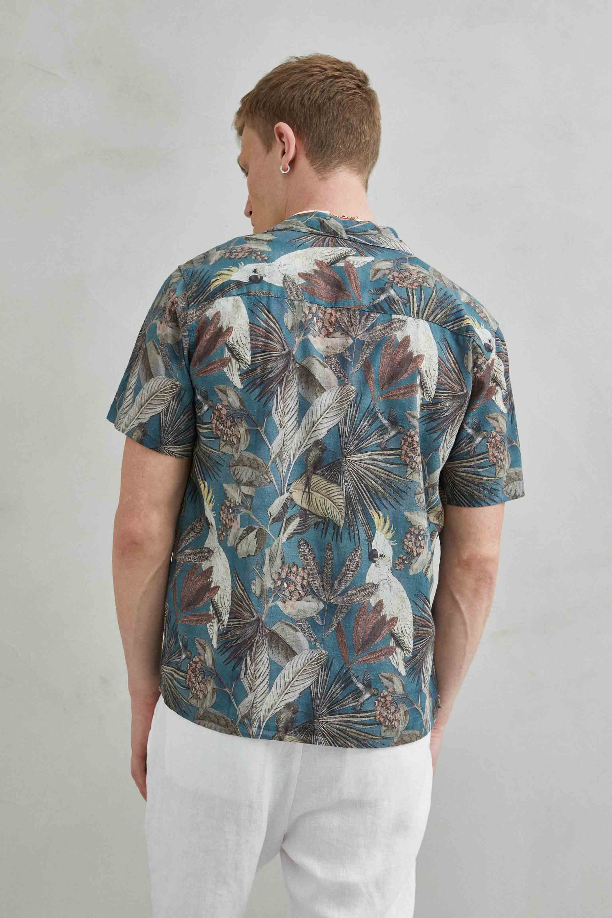Detalle de camisa hawaiana verde con estampado de loro y hojas, hecha de 100% algodón