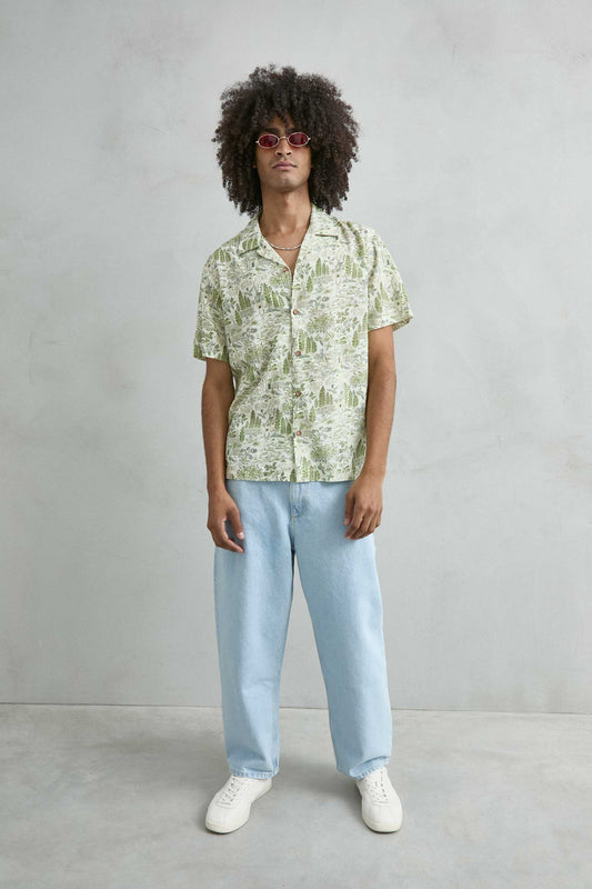 hombre con camisa hawaiana blanca estampada con árboles y cabañas look completo verano