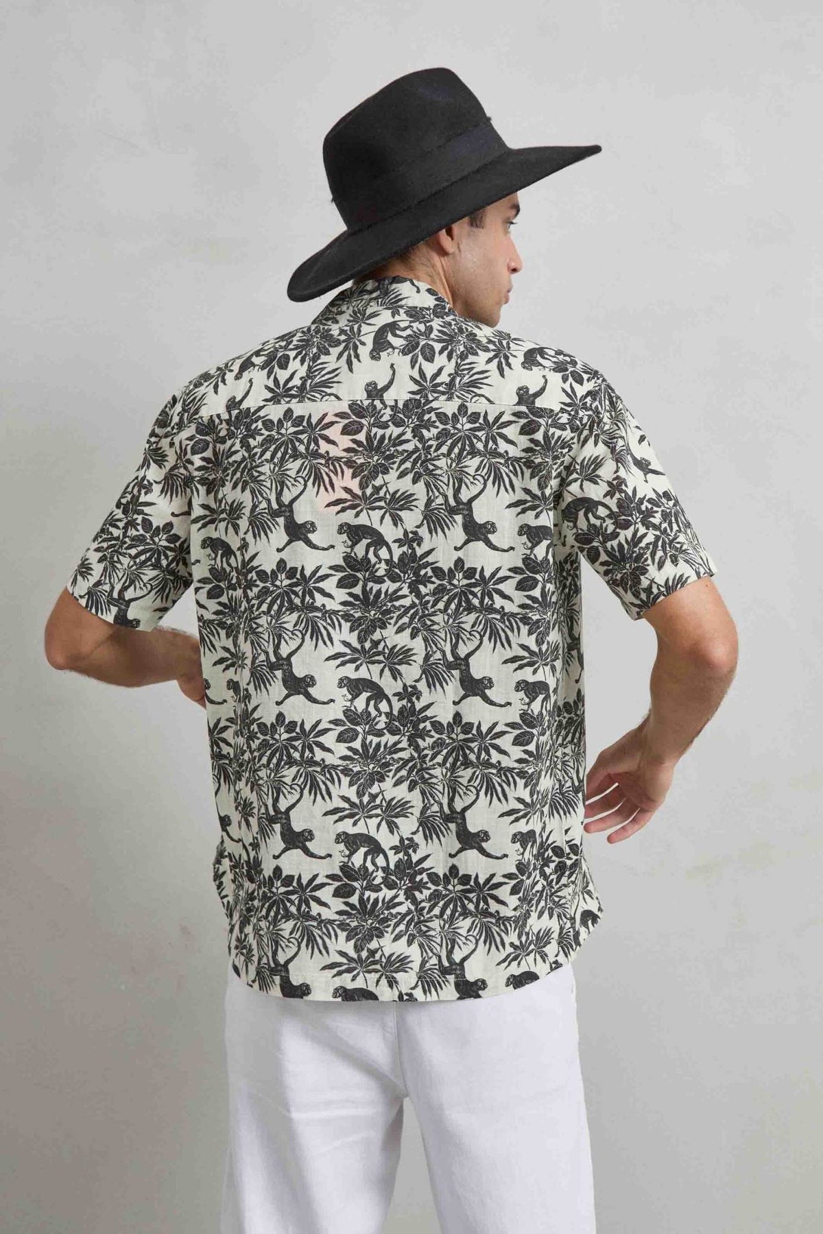 Espalda de camisa de manga corta color crudo con estampado negro de monos y vegetación tropical.