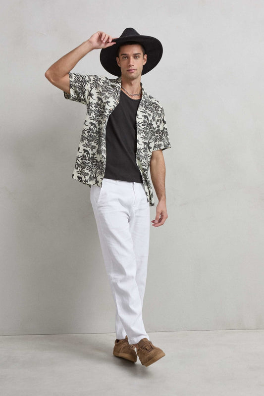 Camisa tropical de manga corta con monos y hojas negras sobre fondo crudo, vista de cuerpo entero.