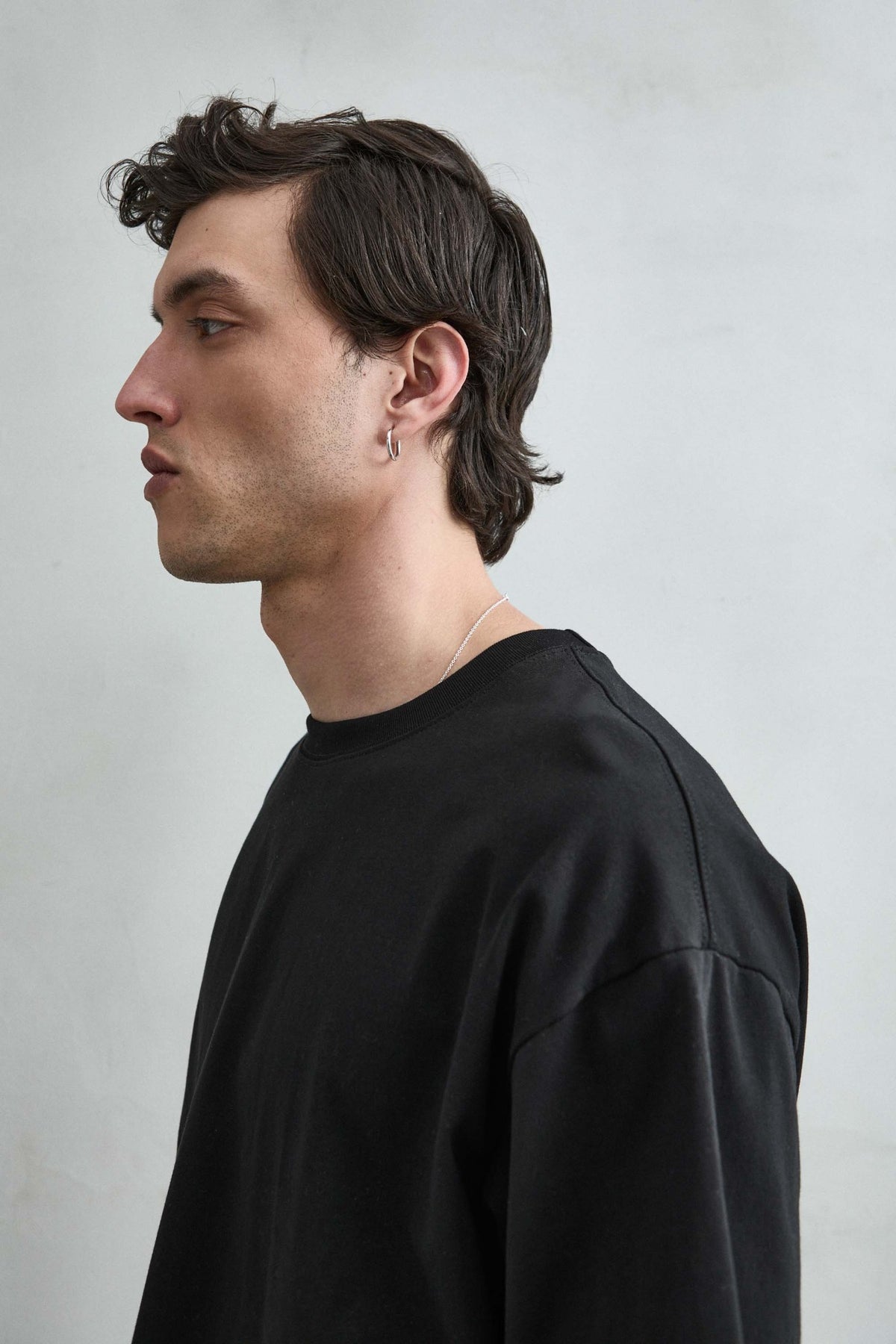 Camiseta cropped oversize negra lisa de hombre, detalle del cuello y manga.