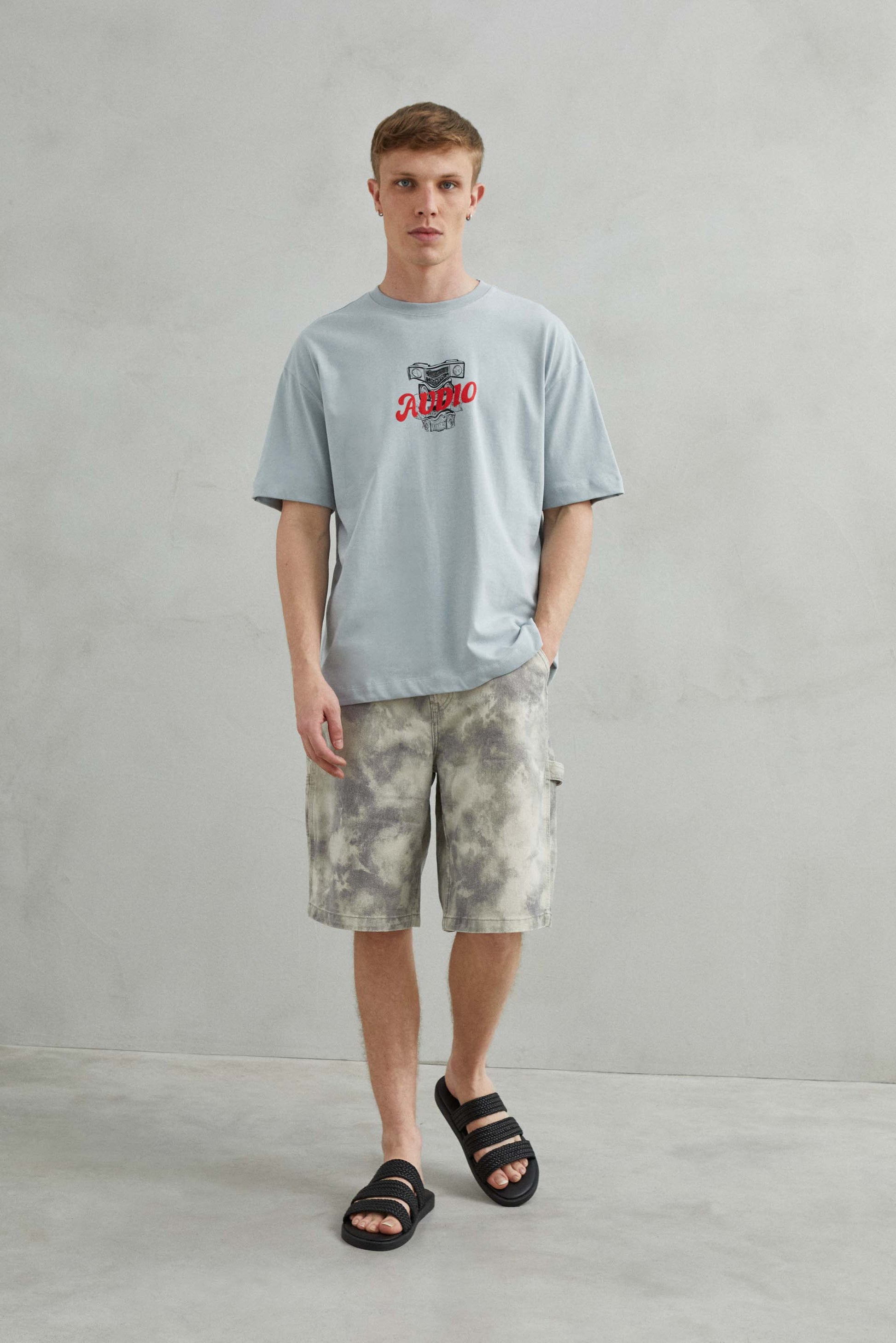 Modelo masculino con camiseta oversize gris "AUDIO", estilo urbano.