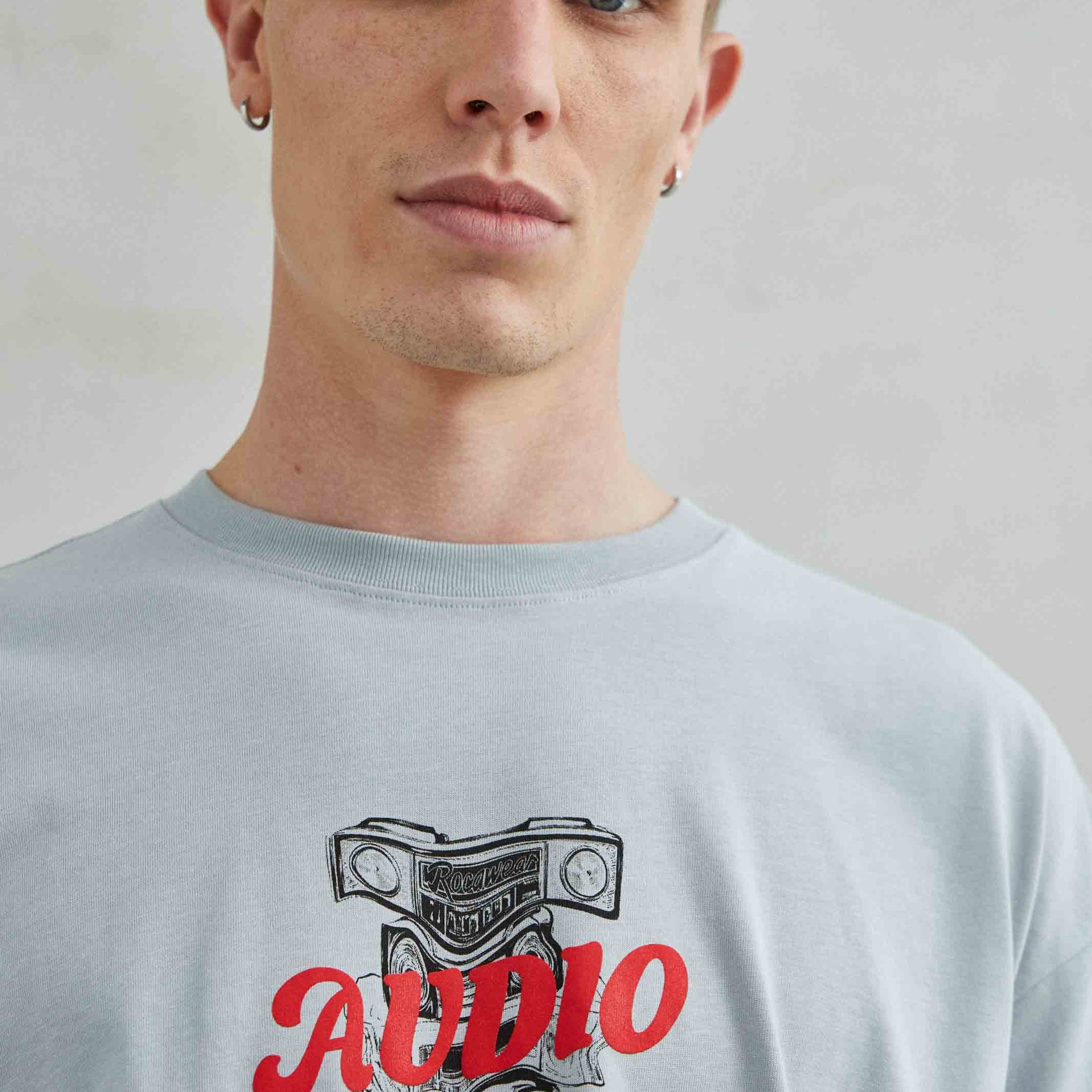 Camiseta oversize unisex gris con diseño gráfico "AUDIO" en el pecho.