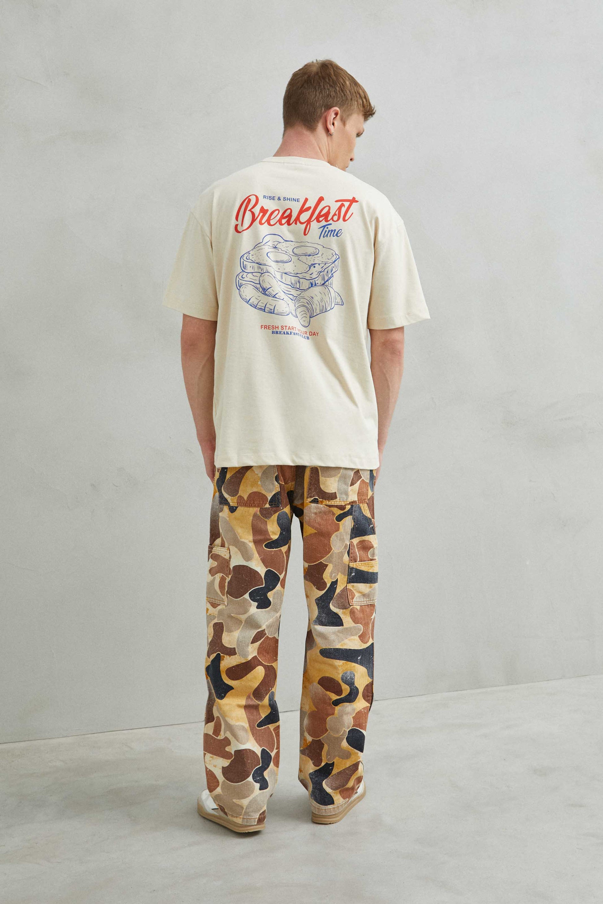  Modelo masculino con camiseta oversize beige "Breakfast y Croissant", estilo urbano.