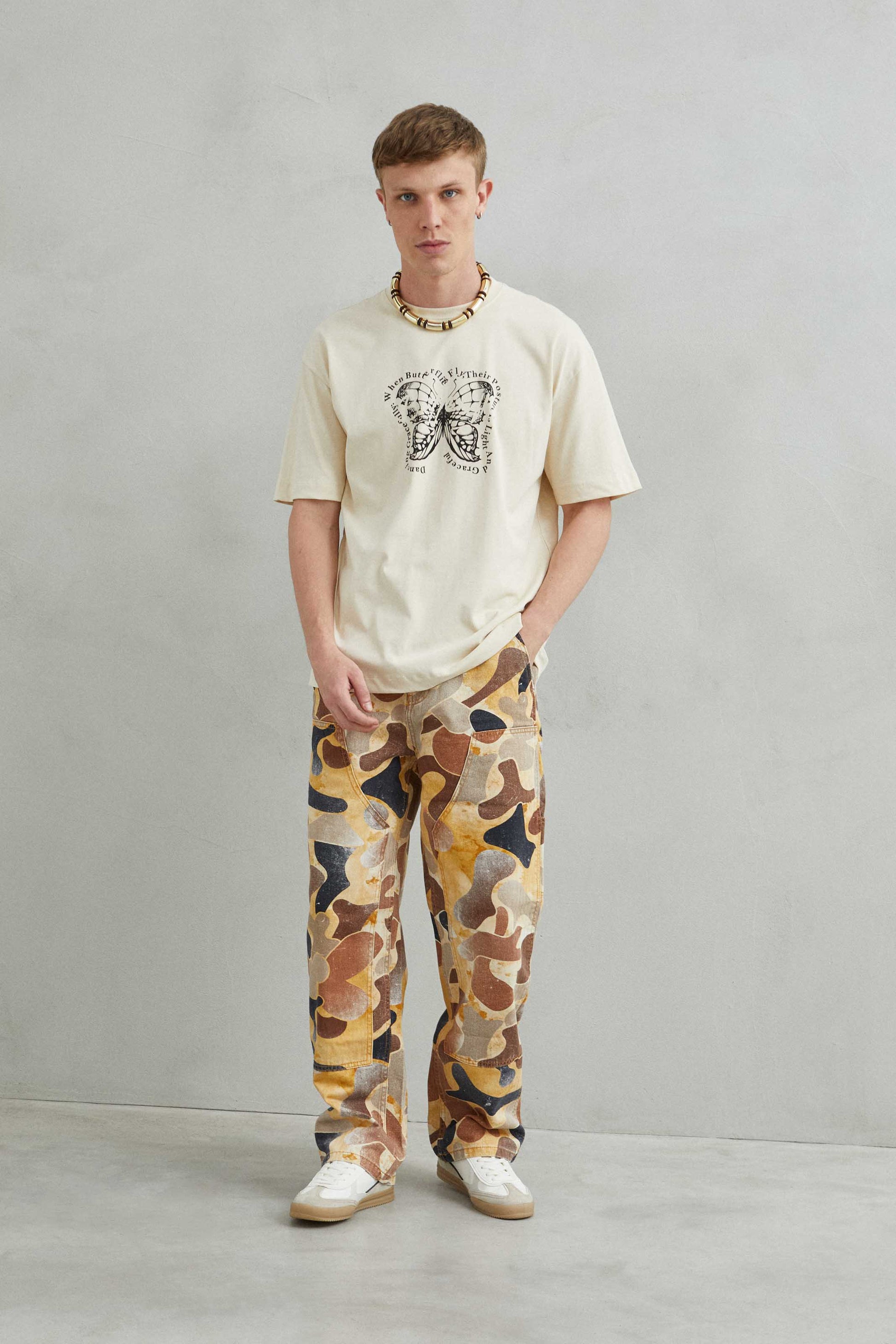 Modelo masculino con camiseta oversize beige con diseño de mariposa, estilo urbano