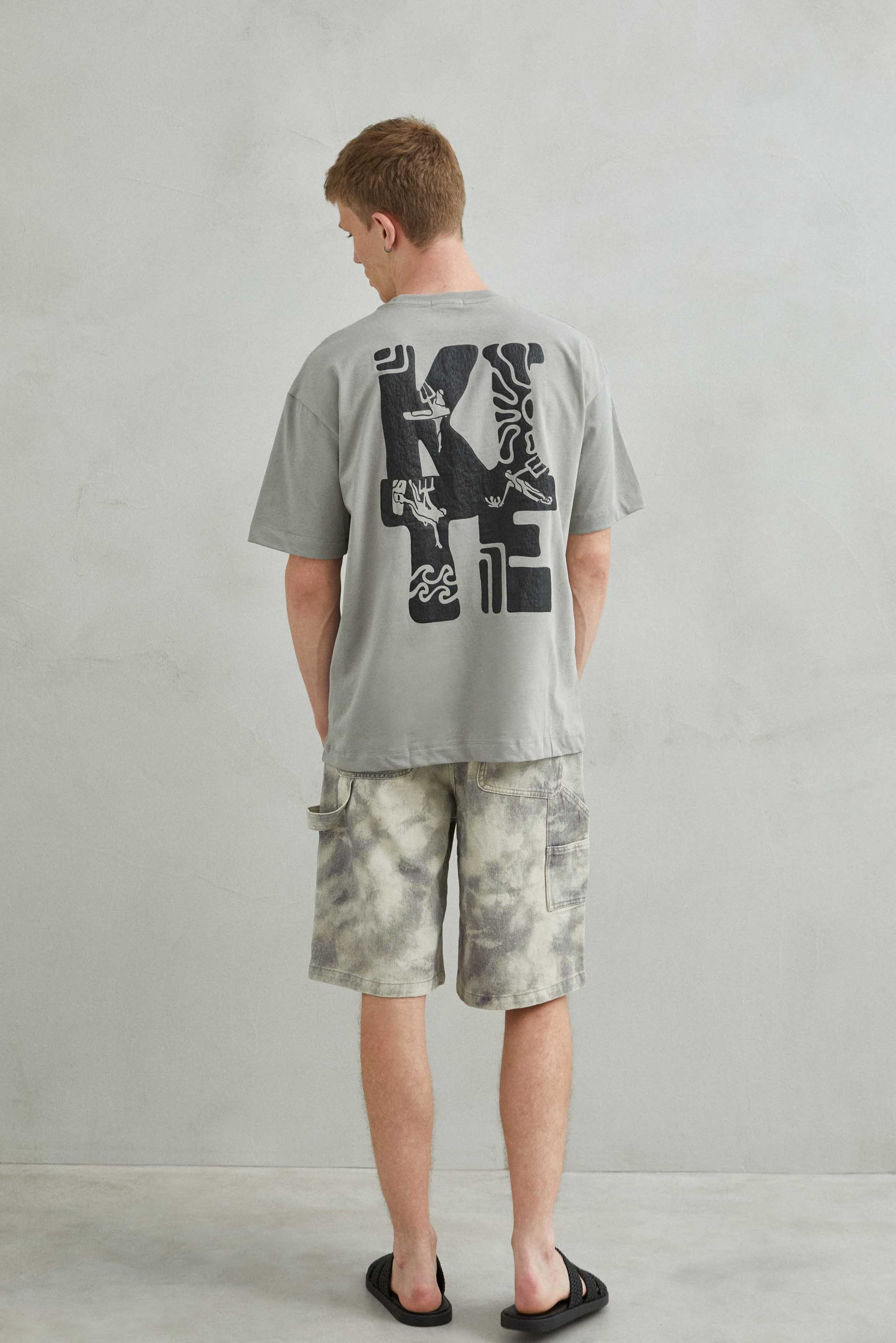 Camiseta gris oversize unisex con diseño kite y patinete estilo skate trasera