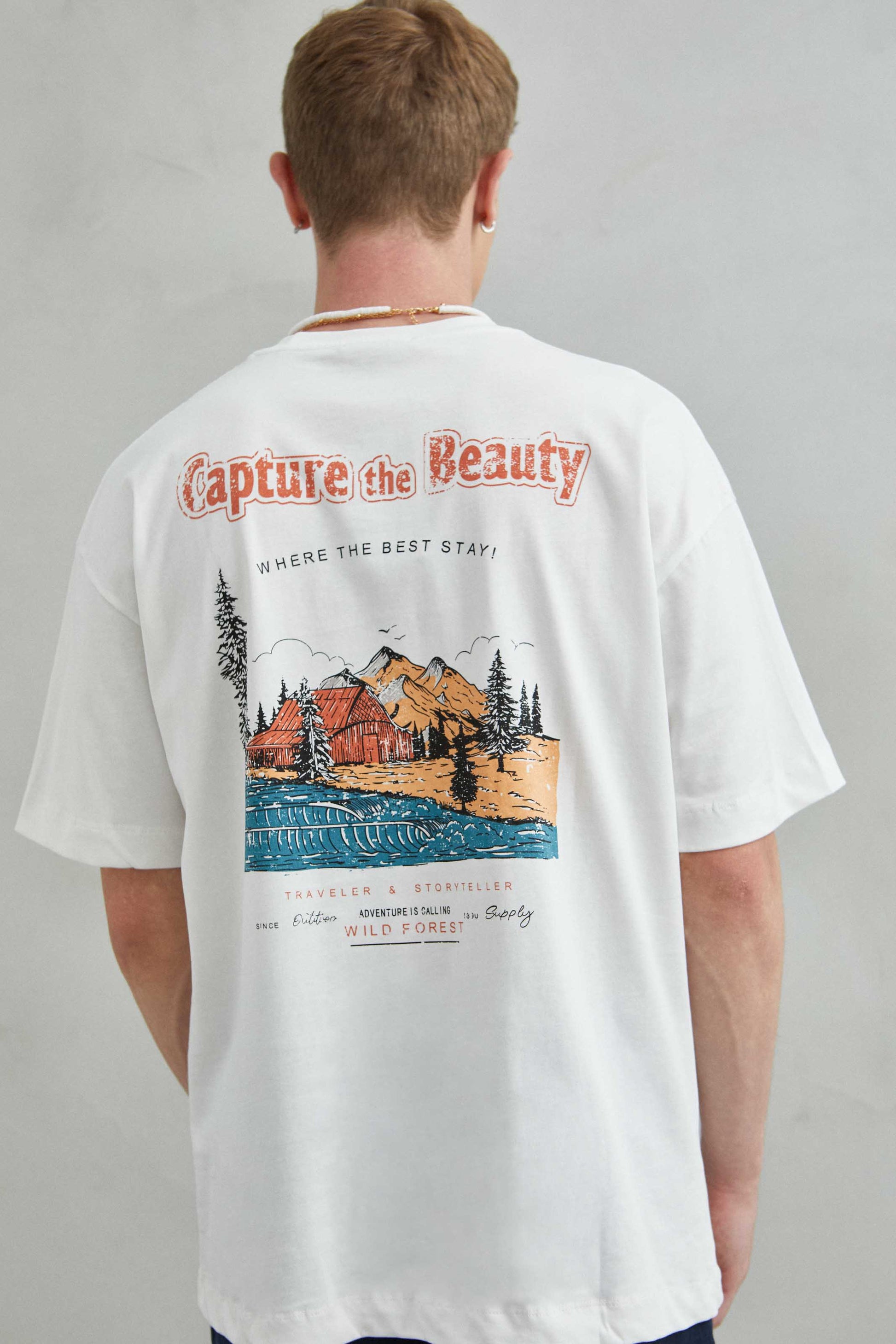 Detalle de la camiseta blanca oversize con diseño de paisaje montañoso en la espalda, estilo naturaleza.