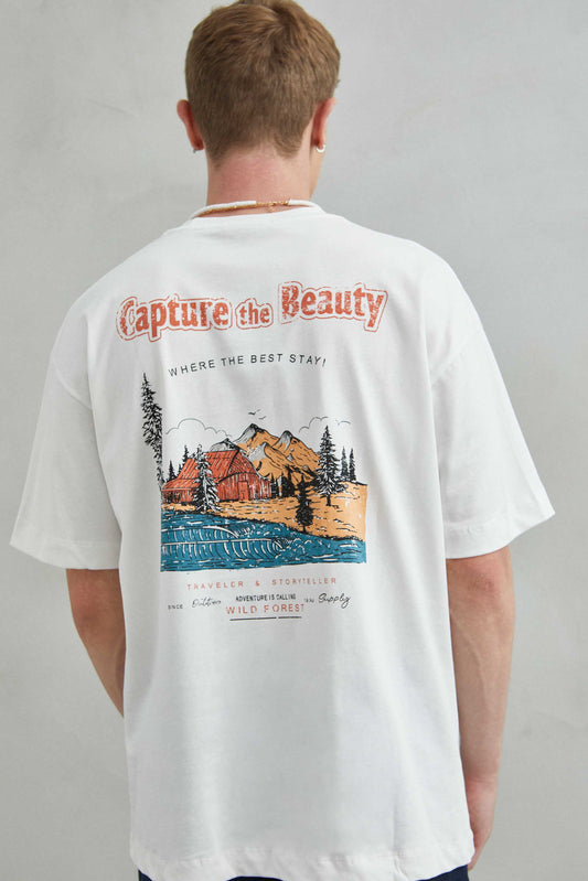 Detalle de la camiseta blanca oversize con diseño de paisaje montañoso en la espalda, estilo naturaleza.