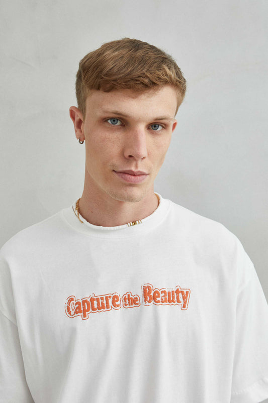 Camiseta blanca oversize unisex con diseño "CAPTURE THE BEAUTY", frente con textura de espuma y diseño natural