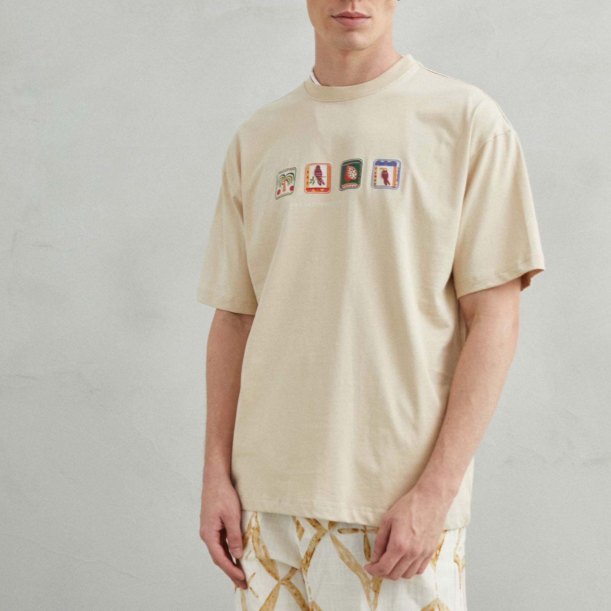  Camiseta beige oversize unisex con diseño en relieve de loro, palmera y frutas tropicales como maracuyá y pitaya.