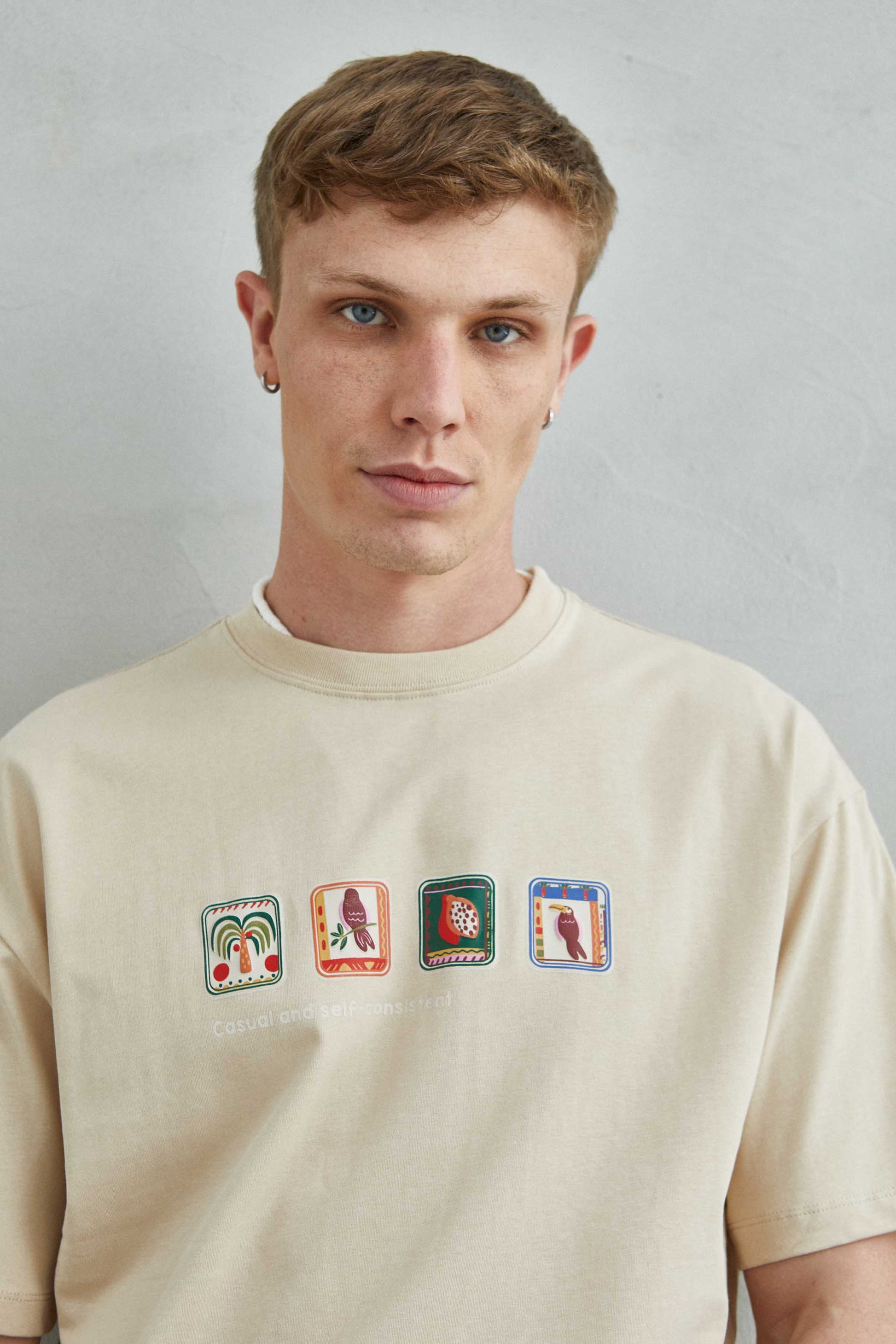 Detalle de la camiseta beige oversize con gráficos de loro, palmera, y frutas tropicales como maracuyá o pitaya.