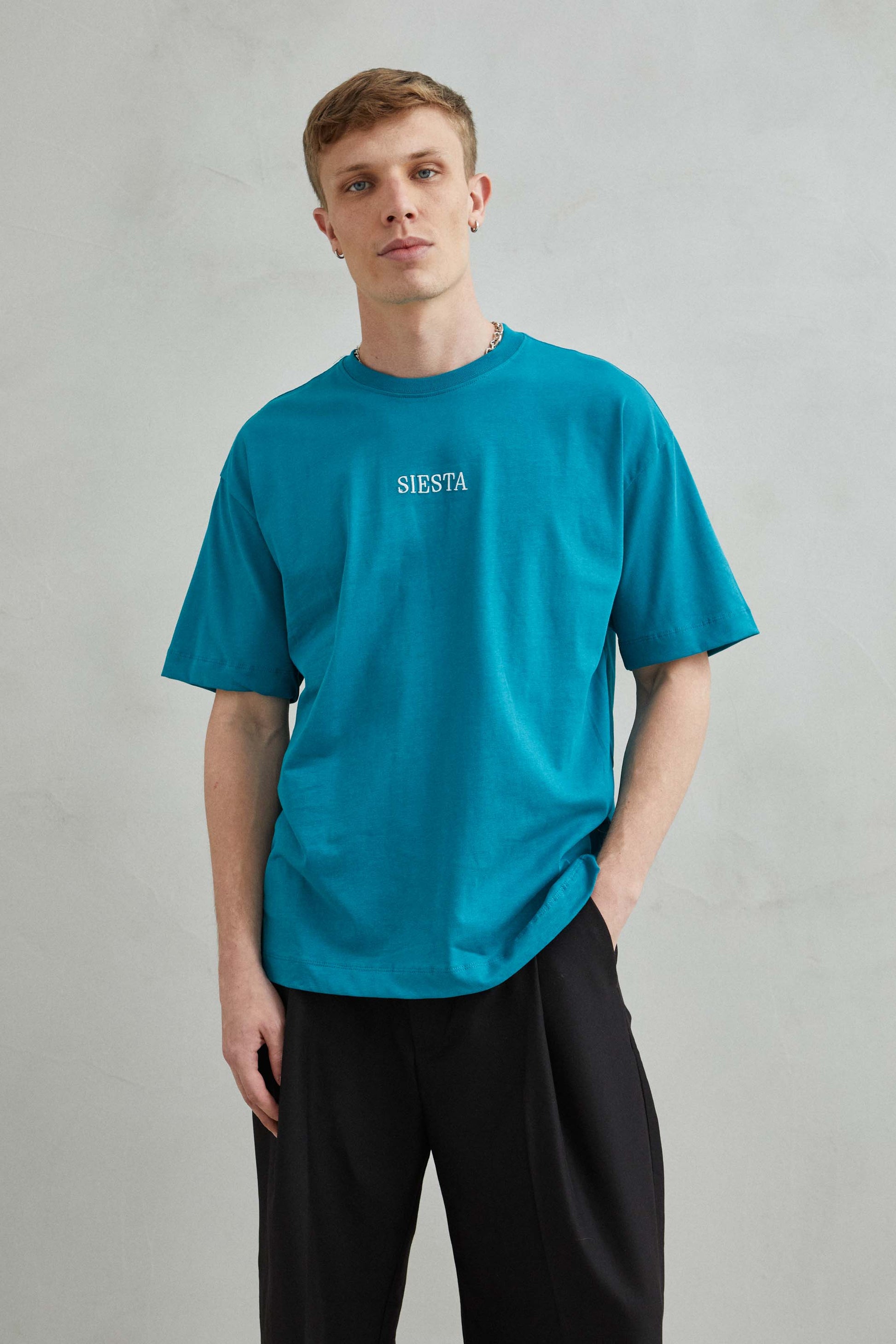 Vista frontal de camiseta verde oversize unisex con texto bordado "Siesta" y koala en siesta