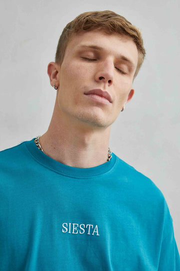 Detalle de camiseta verde oversize con texto bordado "Siesta" y diseño de koala durmiendo