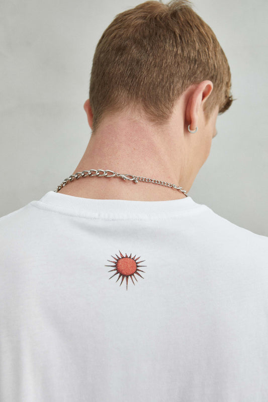 Detalle de camiseta blanca oversize con diseño de "SUNSET" bordado, sol y cactus