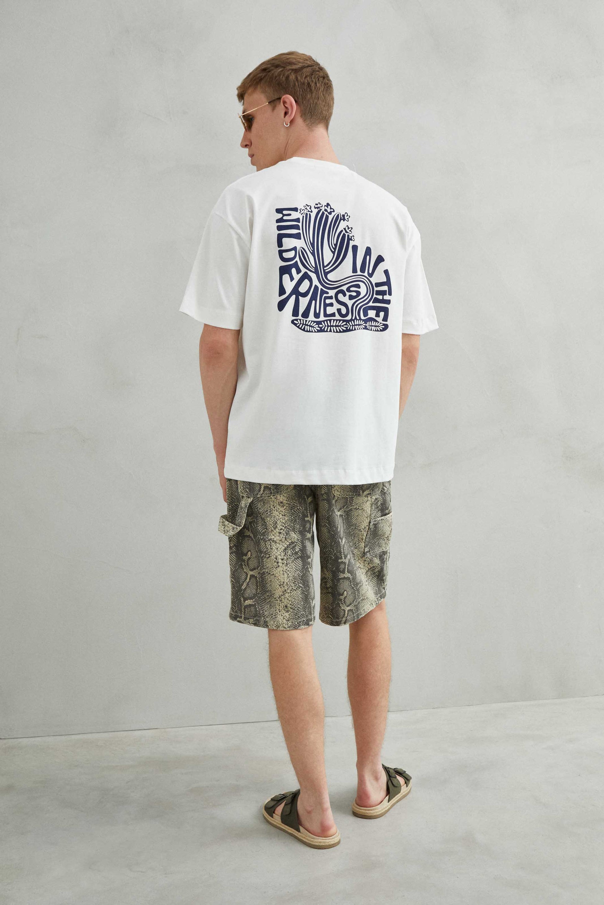 Detalle de camiseta blanca oversize con cactus curvado, texto abstracto y arte de espuma azul