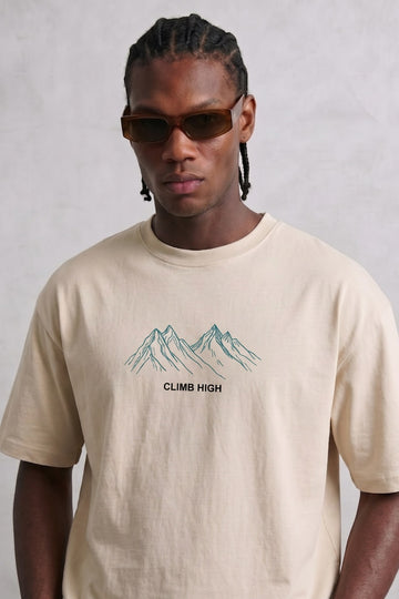 Camiseta oversize beige Climb High con montañas de líneas verde azulado en el pecho, vista frontal.