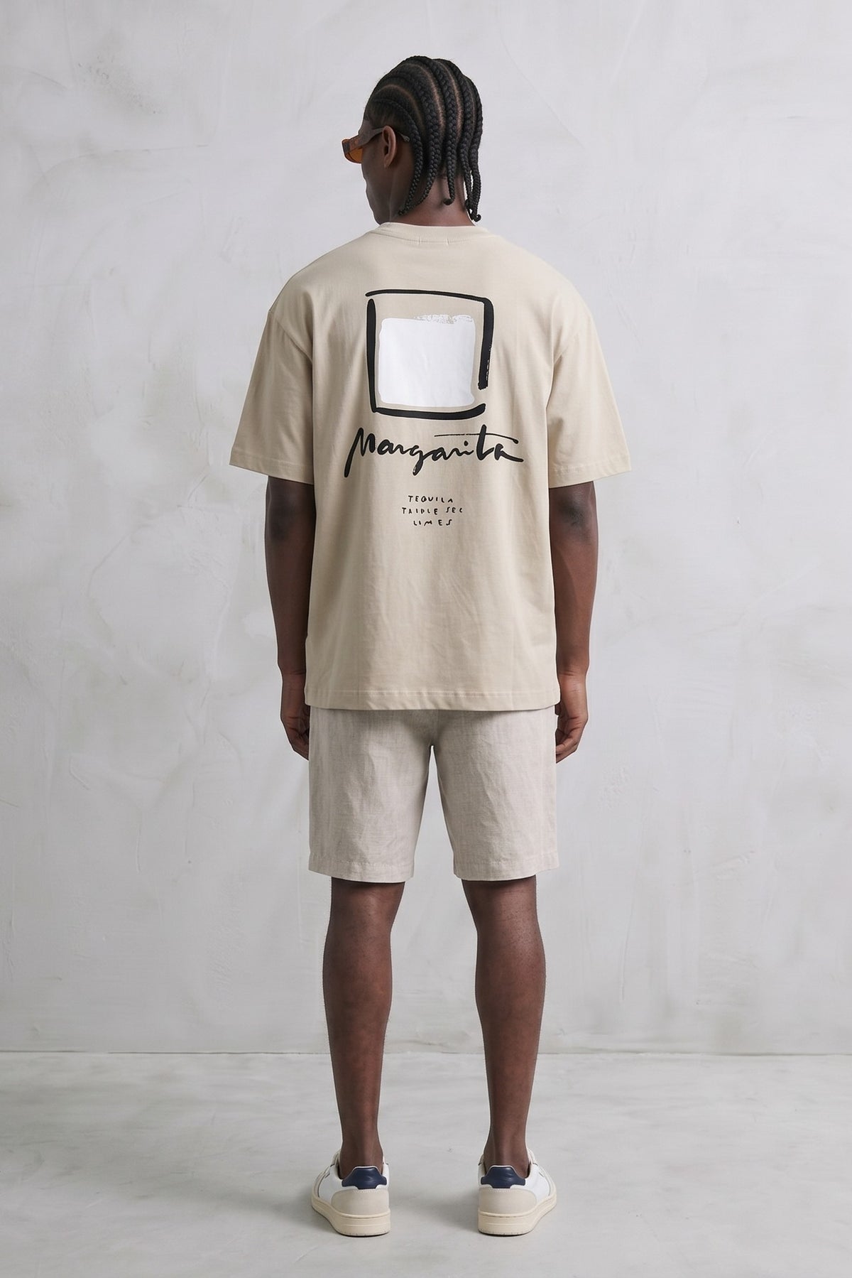 Espalda de camiseta beige con gran cuadrado blanco de borde negro y texto manuscrito.