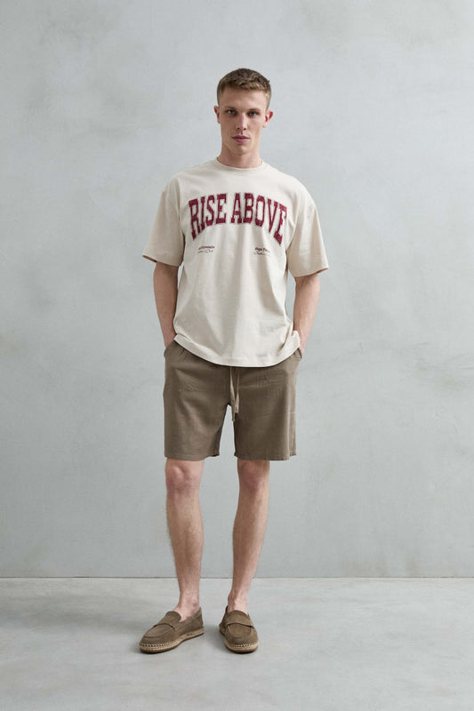 Vista frontal de cuerpo entero de la camiseta oversize beige Rise Above, con hombros caídos, manga corta amplia y bajo recto.
