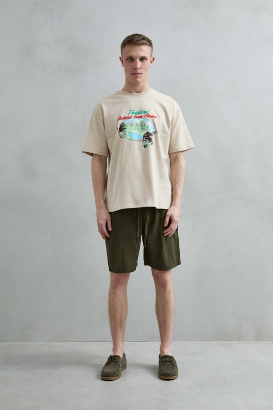 Camiseta oversize beige Thailand Postcard From Phuket con paisaje tropical, mono y tuk tuk, vista de cuerpo entero.