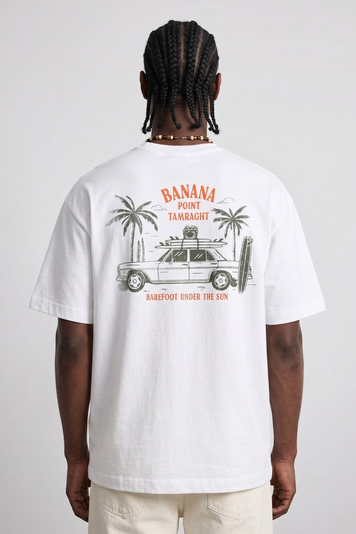 Espalda de camiseta blanca Banana Point Tamraght con coche, tablas de surf y palmeras.