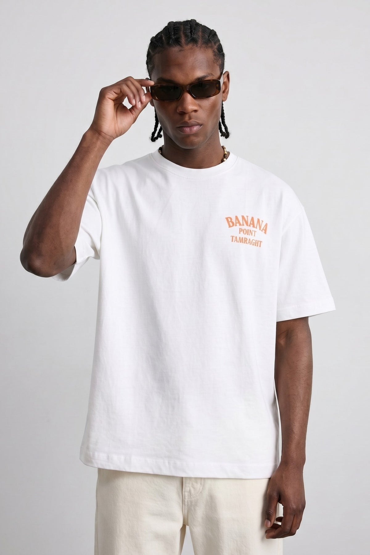 Camiseta oversize blanca Banana Point Tamraght con texto naranja en el pecho, vista frontal.