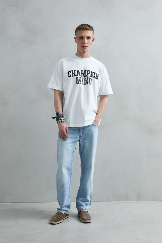 Vista frontal de cuerpo entero de la camiseta oversize blanca Champion Mind para hombre, con letras negras de efecto desgastado en el pecho.