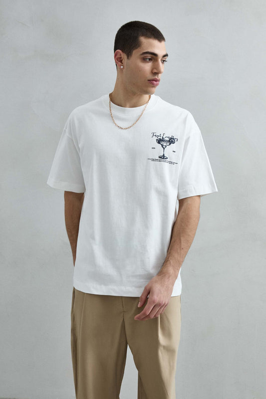 Vista frontal de medio cuerpo de la camiseta oversize blanca Cocktails para hombre, con pequeña copa de cóctel azul marino en el pecho.