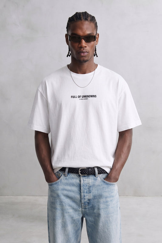 Camiseta oversize blanca Full of Unknowns con pequeño texto negro en el pecho, vista frontal.