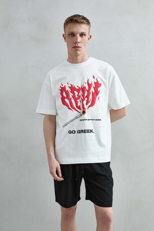 Vista frontal de medio cuerpo de la camiseta oversize blanca Go Greek para hombre, con letras rojas en forma de llamas y una cerilla.