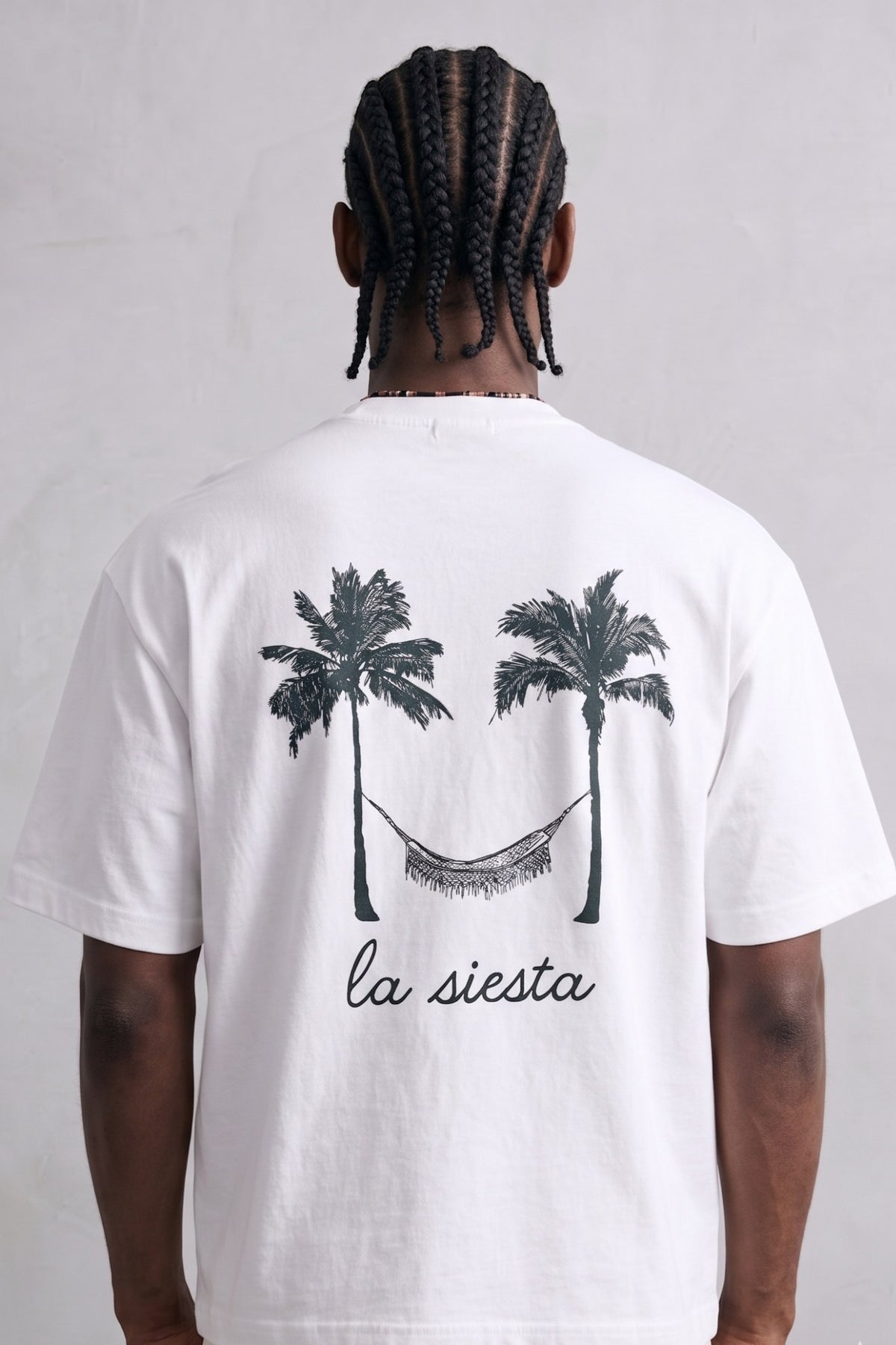 Espalda de camiseta blanca La Siesta con dos palmeras y una hamaca en negro.