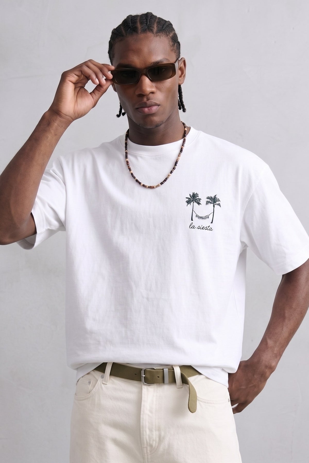 Camiseta oversize blanca La Siesta con pequeño dibujo negro de palmeras y hamaca en el pecho, vista frontal.