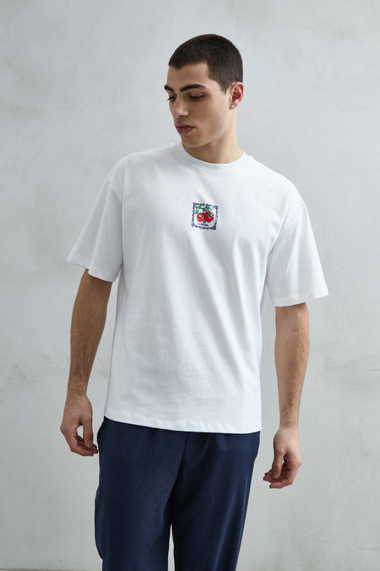Camiseta oversize blanca Le Botanique con pequeño estampado central de tomates rojos y marco azul, vista frontal.