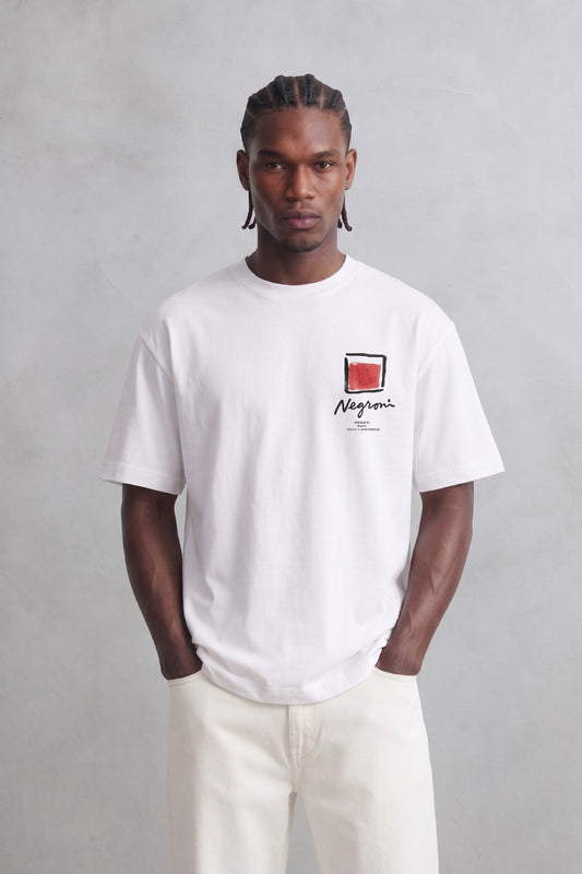 Camiseta oversize blanca Negroni con pequeño gráfico rojo y negro en el pecho, vista frontal.