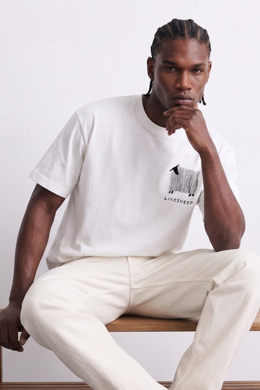 Camiseta oversize blanca con pequeño gráfico negro de oveja y líneas verticales en el pecho, vista frontal.