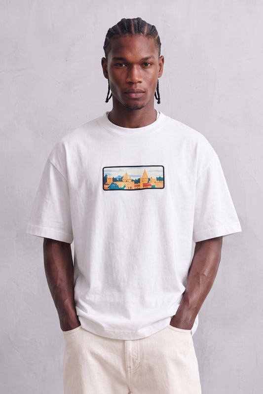 Camiseta oversize blanca con ilustración rectangular de paisaje urbano en naranja y azul, vista frontal.