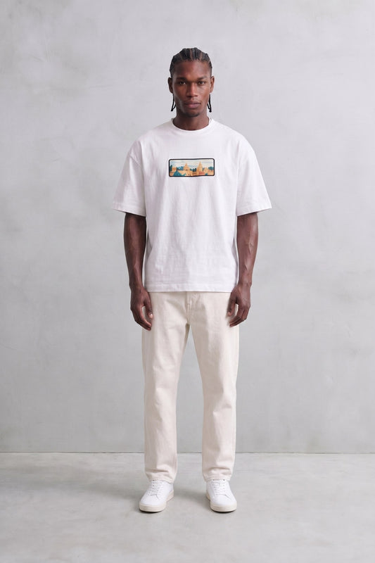 Camiseta oversize blanca con paisaje urbano multicolor en el pecho, vista de cuerpo entero.