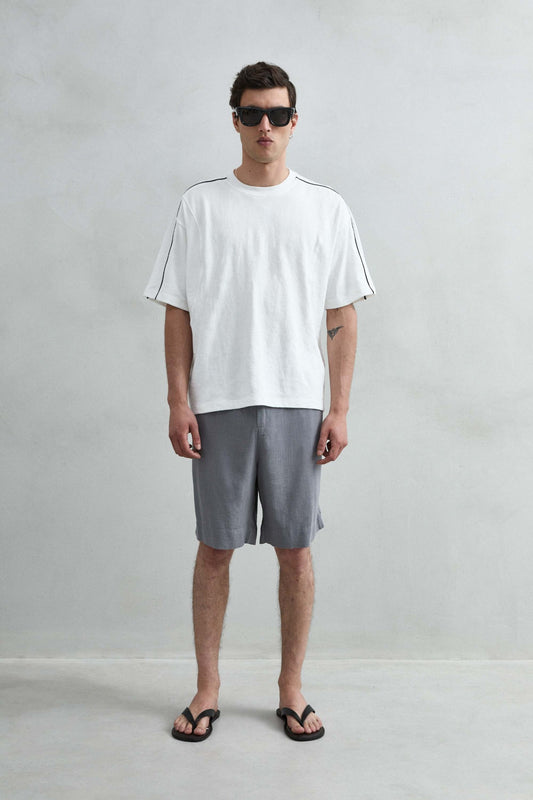 Camiseta oversize blanca de hombre con líneas negras en hombros y mangas, vista de cuerpo entero.
