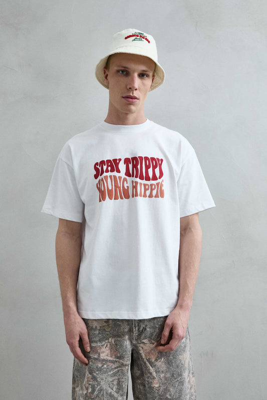 Camiseta oversize blanca Stay Trippy con letras retro rojas y naranjas en el pecho, vista frontal.