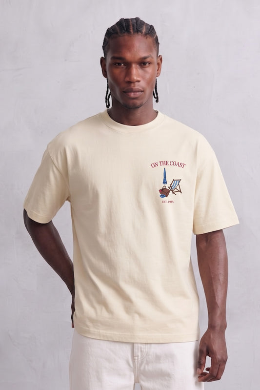 Camiseta oversize crema On The Coast con pequeño motivo de silla de playa y sombrilla en el pecho, vista frontal.