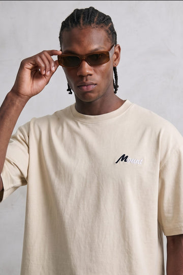 Camiseta oversize color crema con pequeño texto en el pecho, vista frontal.