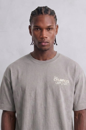 Camiseta oversize gris The Churros Complot con pequeño texto claro en el pecho, vista frontal.