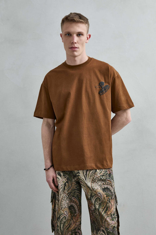 Vista frontal de medio cuerpo de la camiseta oversize marrón Duck Records para hombre, con pequeño gráfico negro de pato y disco en el pecho.