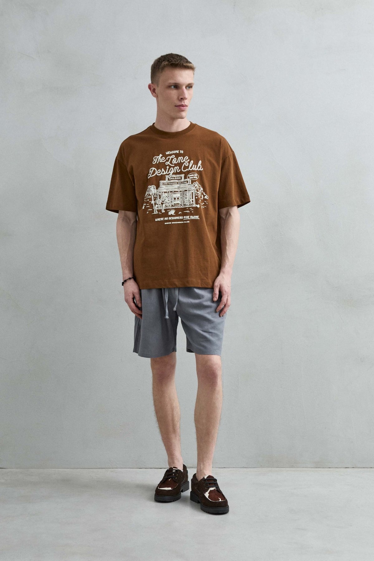 Vista frontal de cuerpo entero de la camiseta oversize marrón The Lone Design Club para hombre, con manga corta amplia y hombros caídos.