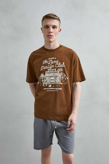 Vista frontal de medio cuerpo de la camiseta oversize marrón The Lone Design Club, con ilustración clara de un saloon del Oeste.
