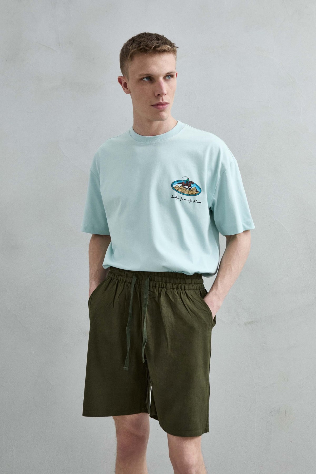 Vista frontal de medio cuerpo de la camiseta oversize verde menta Rusher from the Dust para hombre, con pequeño motivo de jinete y pirámides en el pecho.
