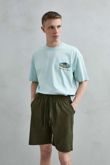 Vista frontal de medio cuerpo de la camiseta oversize verde menta Rusher from the Dust para hombre, con pequeño motivo de jinete y pirámides en el pecho.