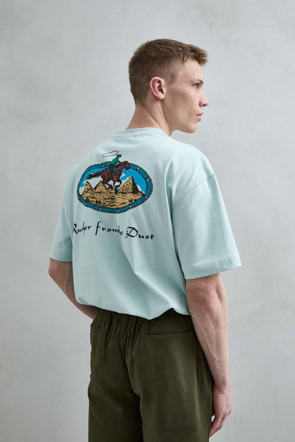 Vista trasera de la camiseta oversize verde menta Rusher from the Dust, con gran ilustración ovalada de jinete a caballo y pirámides.