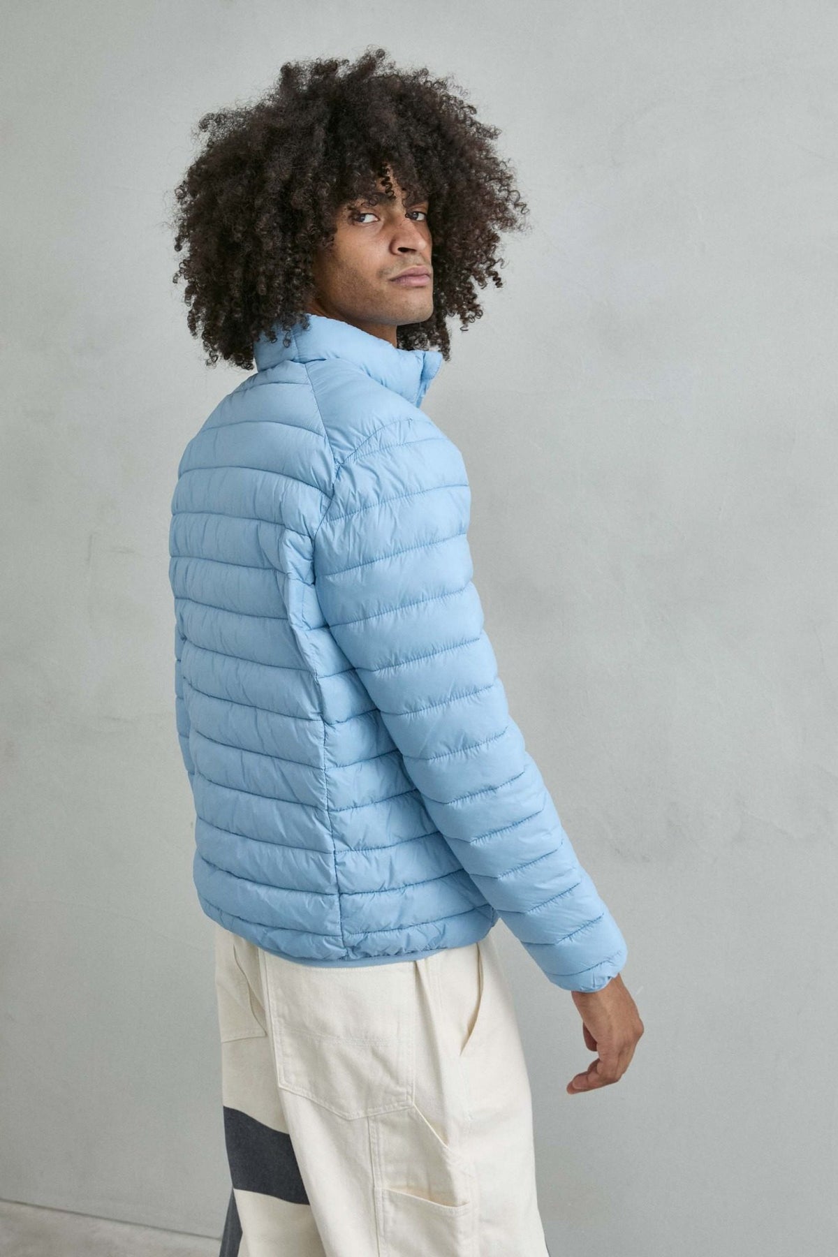 Chaqueta acolchada de hombre azul cielo con cuello alto y cremallera de doble cursor, vista espalda.